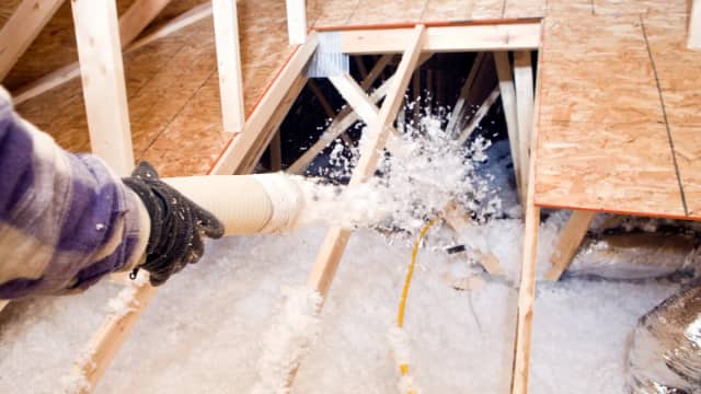 Hose blowing loose-fill insulation into attic floor joists in Rochester MN