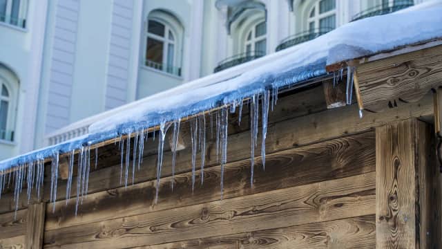 Ice dam forming along the edge of a snow-covered house roof